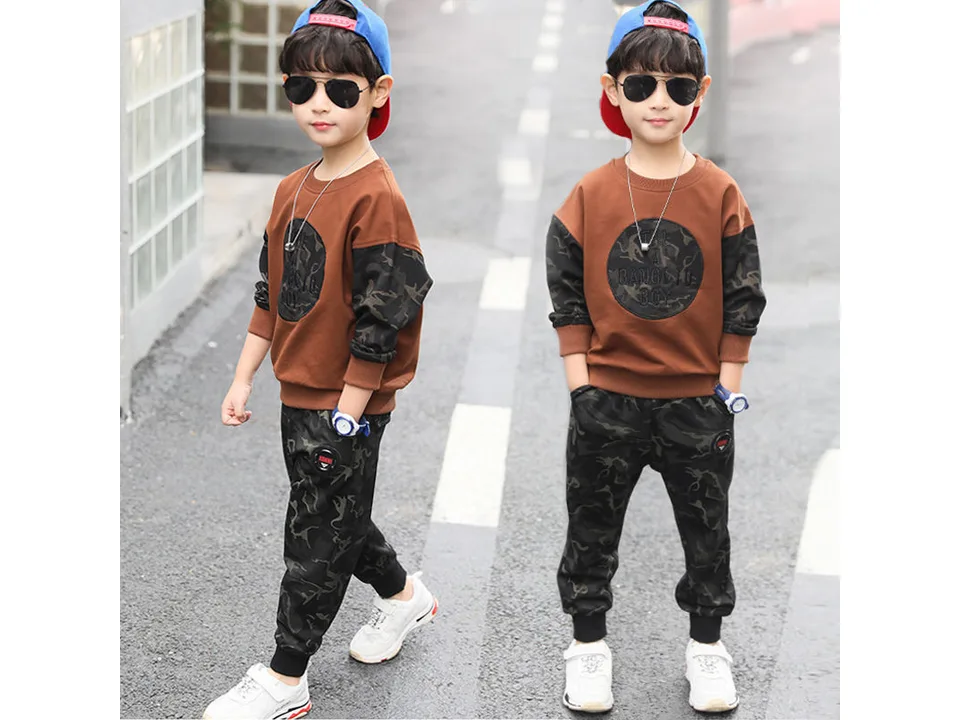 A boy wearing a brown long-sleeved shirt with camouflage sleeves and matching camouflage pants.