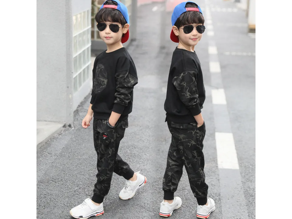 A boy wearing a black long-sleeved shirt with camouflage sleeves and matching camouflage pants.