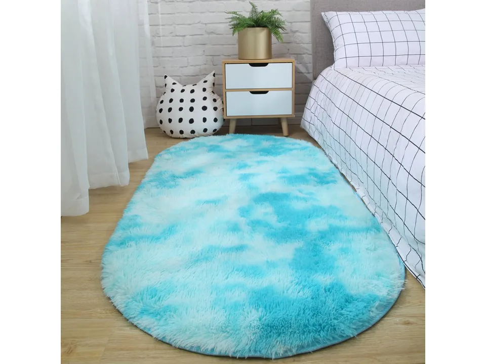 A bright blue oval shaggy rug placed on a wooden floor next to a bed.