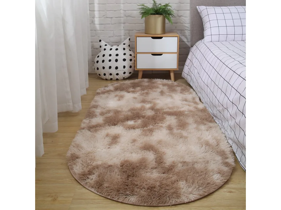 A light brown oval shaggy rug placed on a wooden floor next to a bed.