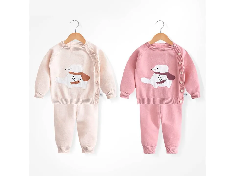 Two infant knitted sweater and pants sets in beige and pink on hangers.