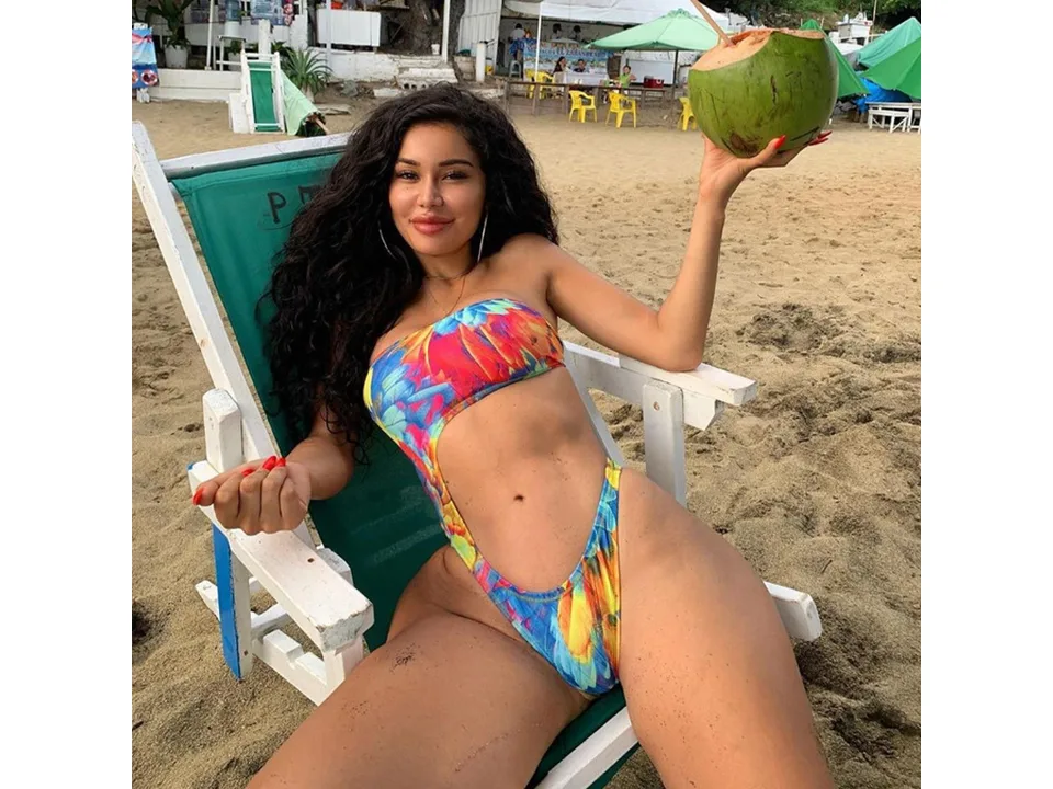 A woman wearing a floral print cutout one-piece swimsuit sitting on a beach chair.
