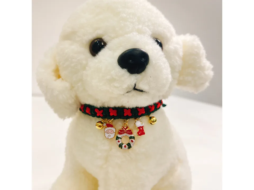A white plush dog wearing a green and red braided Christmas collar with festive charms.