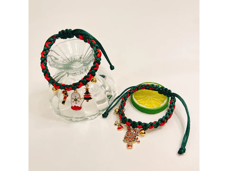 Two braided Christmas pet collars with festive charms displayed next to a glass vase and a lime slice.