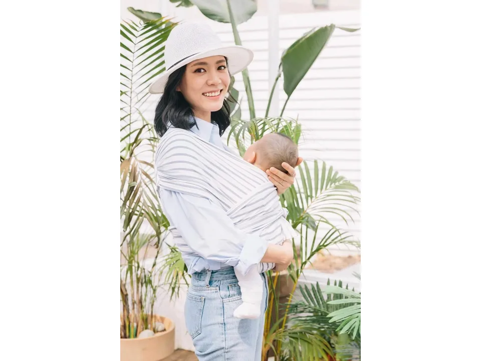 A woman wearing a striped baby sling carrier with a baby, showing how it fits.