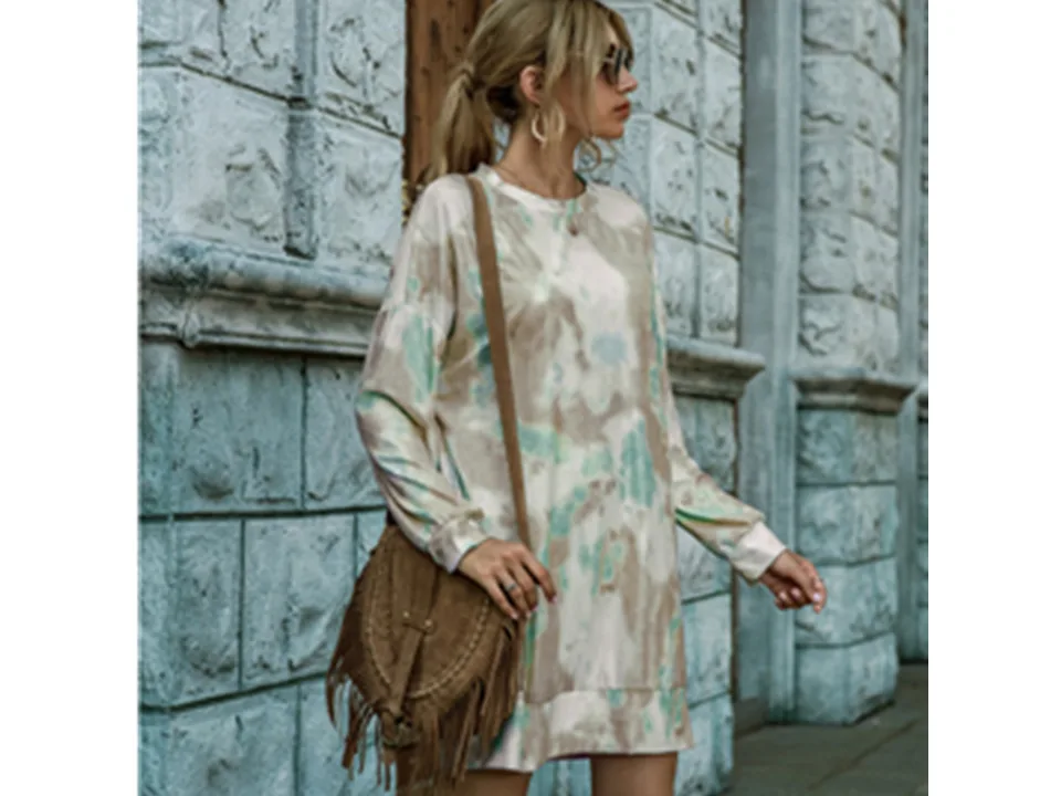 Model wearing a beige and green tie-dye long sleeve sweater dress with a brown fringe bag.