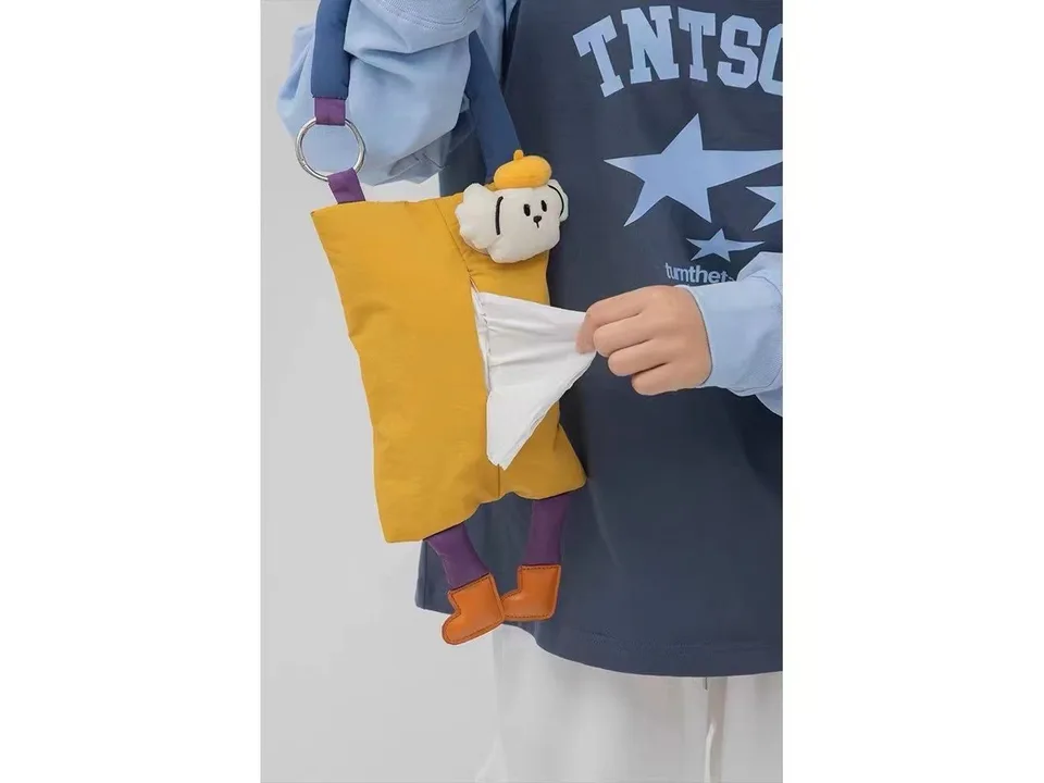 Person holding a yellow plush animal tissue holder with a tissue being pulled out.