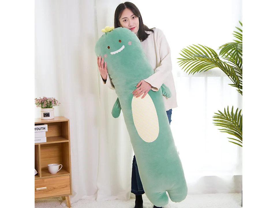 A woman holding a long, green dinosaur-shaped plush pillow.