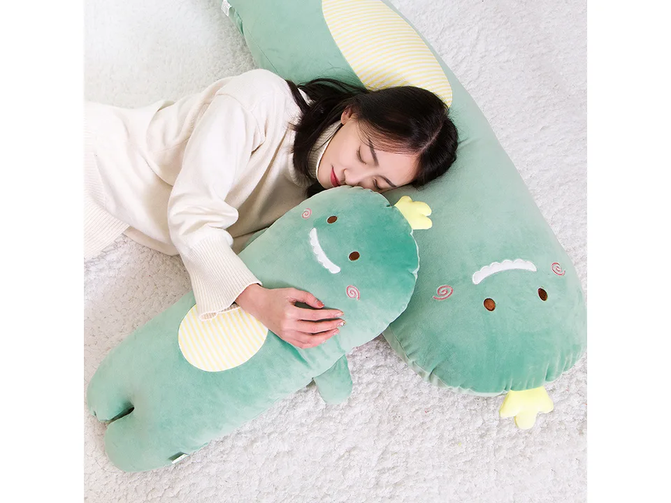 A woman lying down and hugging a long, green dinosaur-shaped plush pillow.