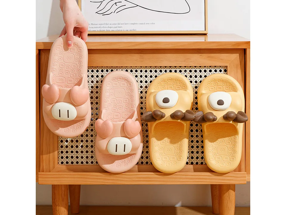A hand holding up a pink pig slipper next to other animal-themed slippers on a wooden shelf.