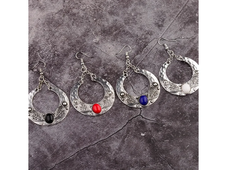 Four pairs of bohemian crescent earrings in different colors arranged on a textured surface.