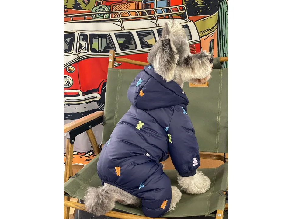 A dog wearing a navy blue hooded jacket with colorful bear embroidery, viewed from the side.