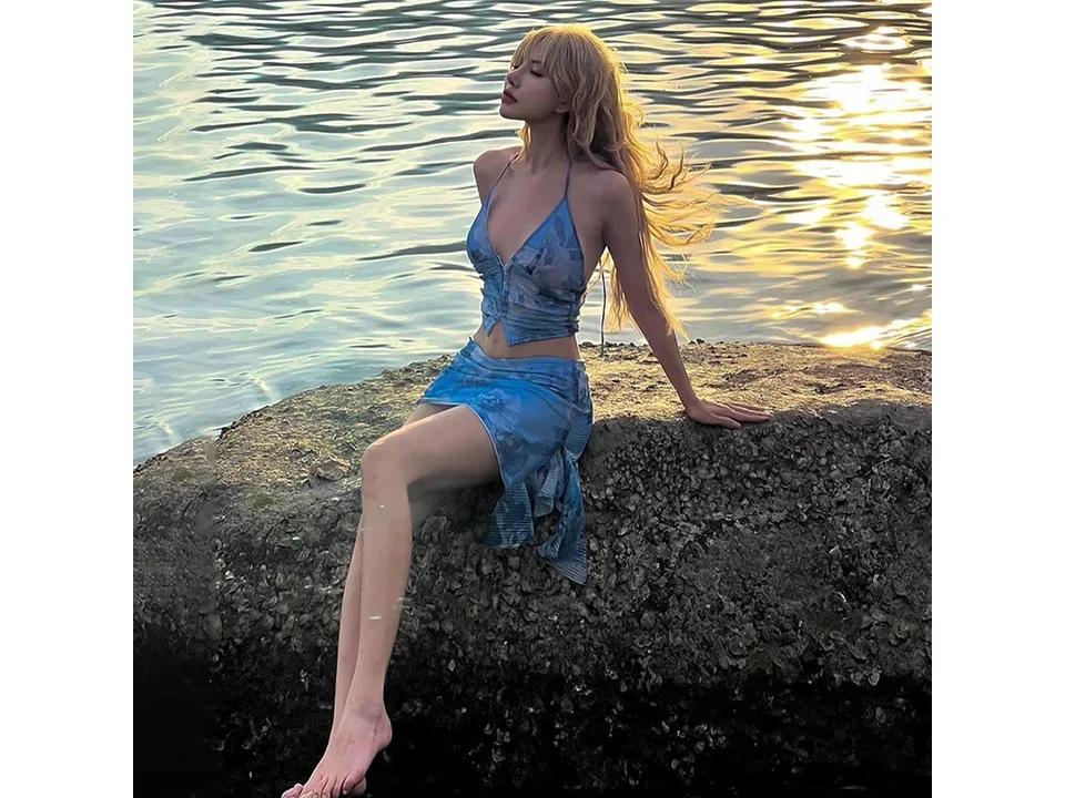A woman sitting on a rock by the water wearing a blue floral two-piece set.