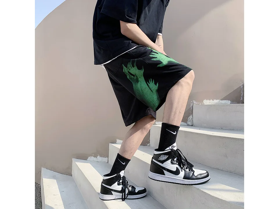 A person wearing black shorts with a green hand graphic, standing on stairs.