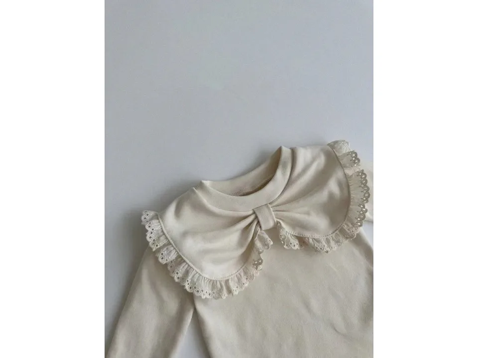 Close-up of a cream-colored long-sleeve blouse with a large lace-trimmed bow collar.