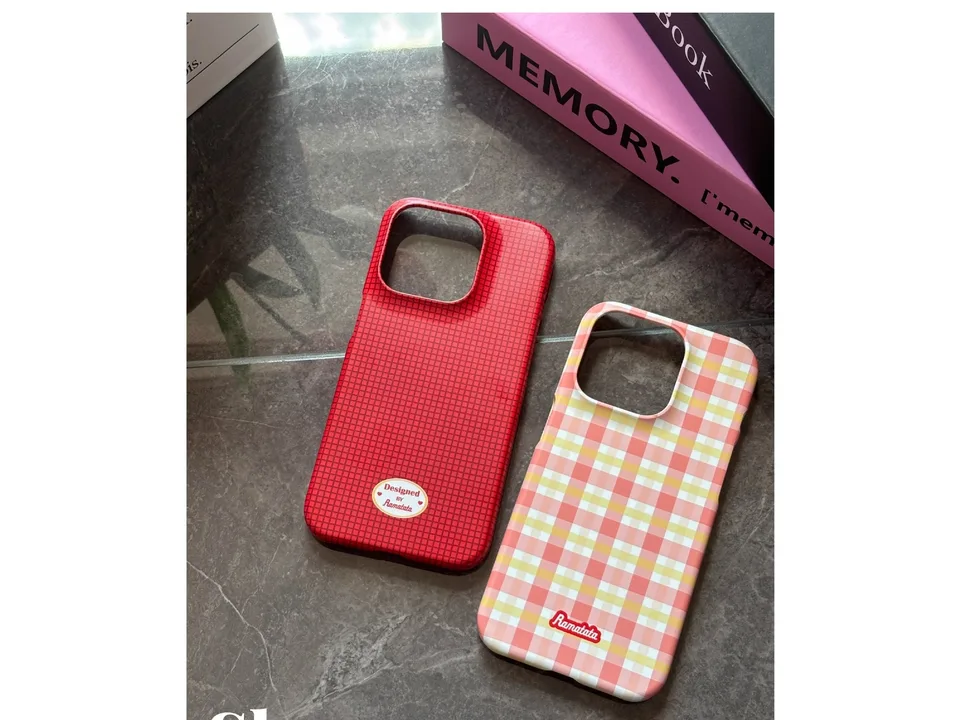 Red grid and pink plaid phone cases lying on a dark surface.