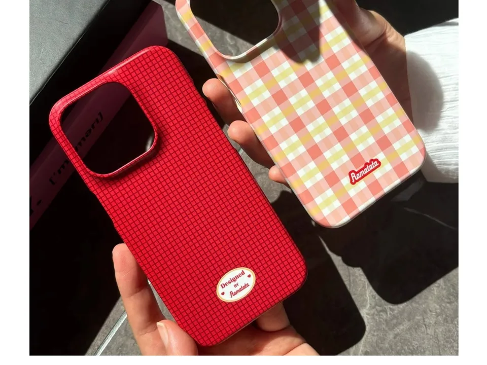 Two phone cases, one red grid and one pink plaid, held in a hand.