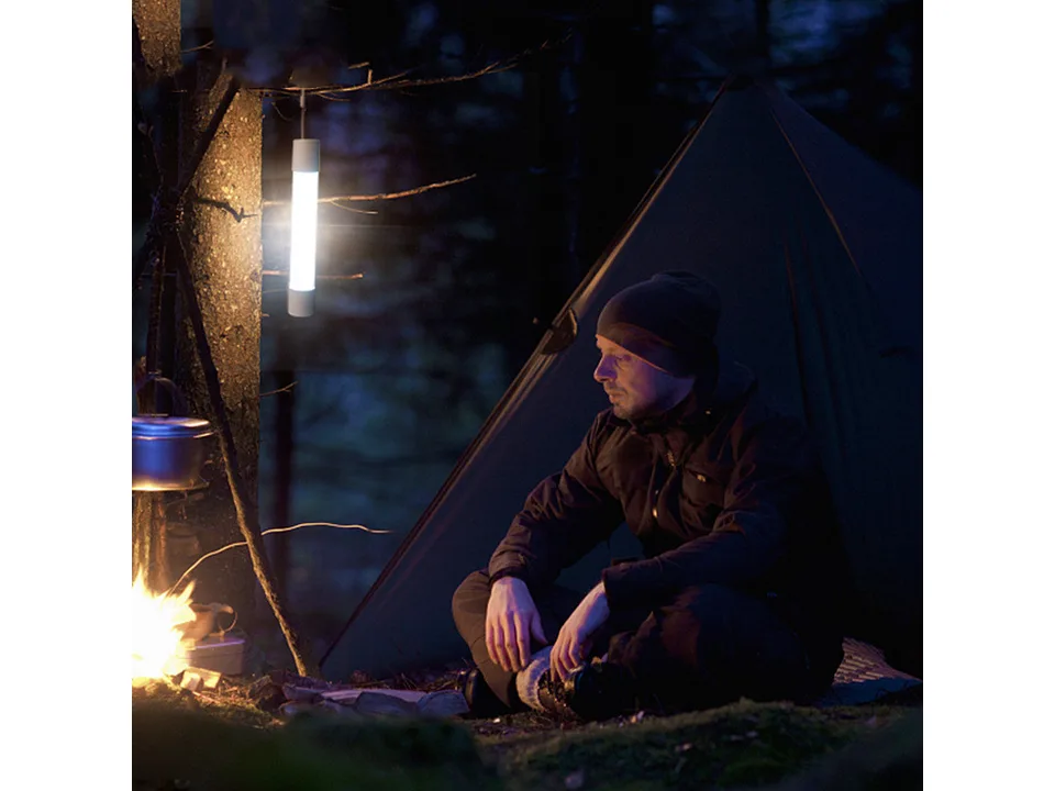 A person sitting in a tent at night with the LED tube light hanging from a tree branch.