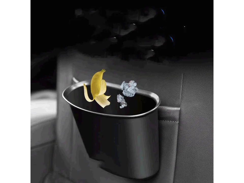 A black car trash can hanging on the back of a car seat with trash inside.