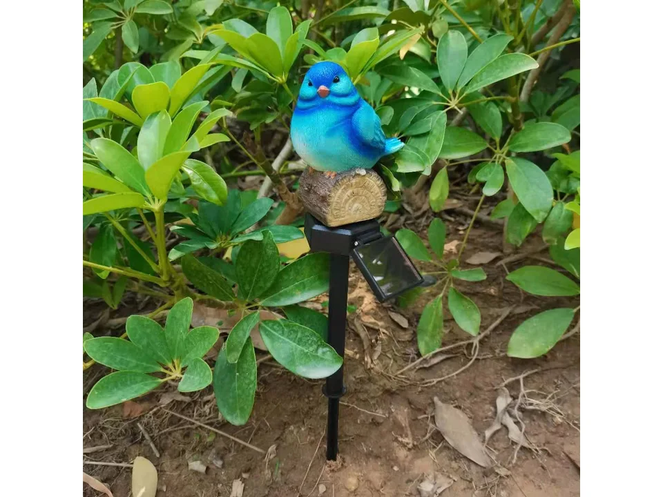 A blue bird garden stake light with a solar panel, installed in a garden.