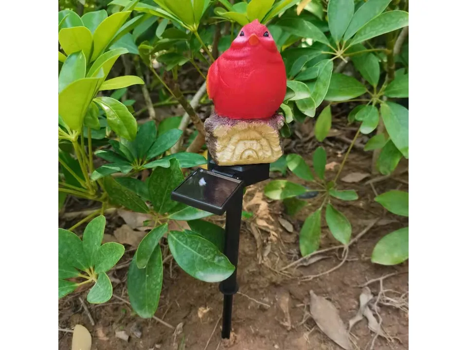 A red bird garden stake light with a solar panel, installed in a garden.