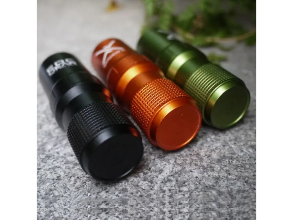 Three survival storage capsules in black, orange, and green standing on a textured surface.