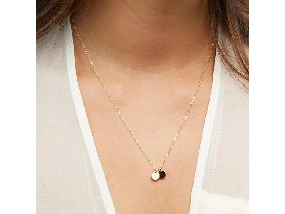 A gold necklace with two small round pendants worn on a person.