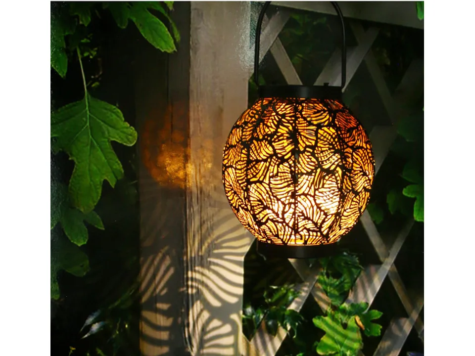 A decorative metal lantern hanging in a garden, casting a leaf-patterned shadow.