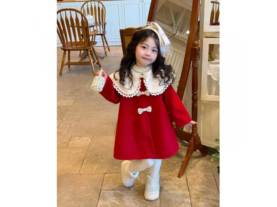 A young girl wearing a red winter coat with a large white collar and pearl bow details.