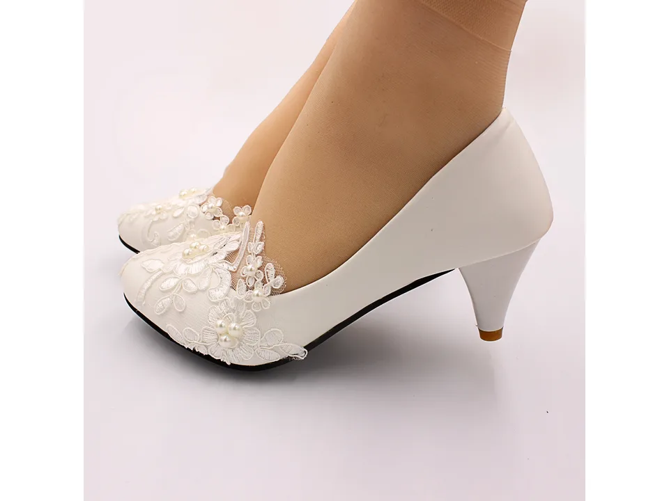 Close-up of a person wearing white lace wedding shoes.