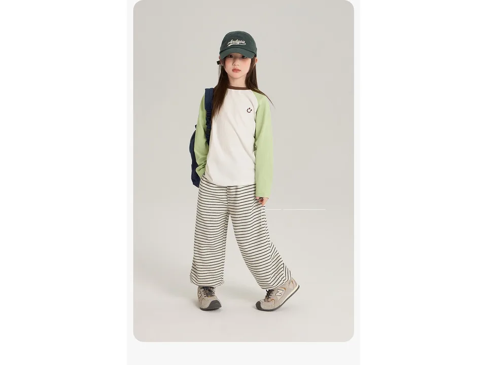 A girl wearing a white and green long-sleeve top with a small smiley face graphic.