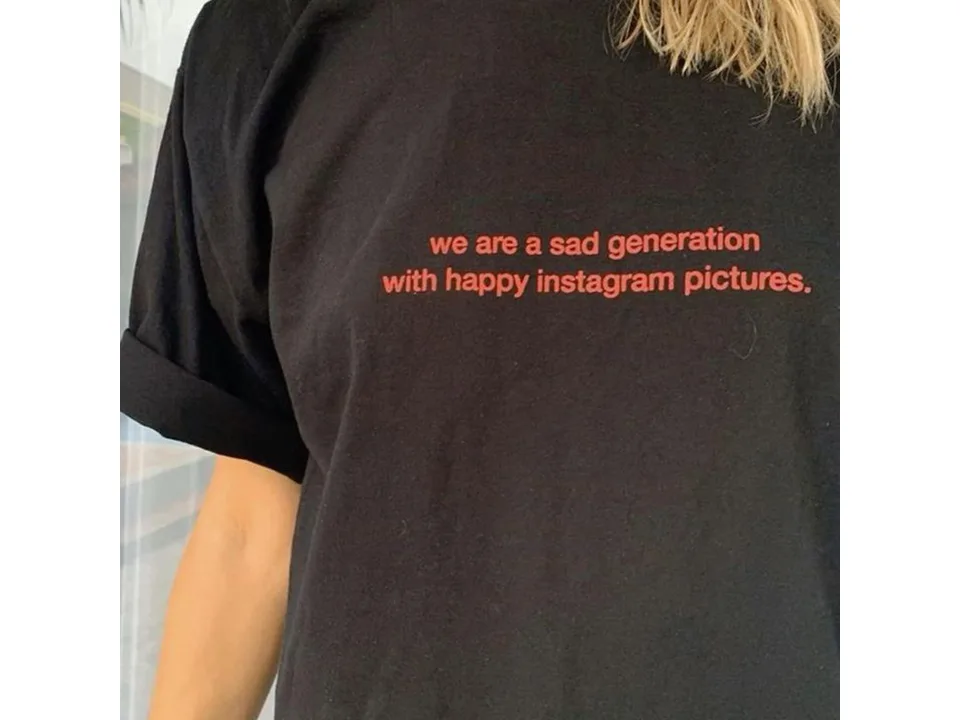 Close-up of a black t-shirt with the text 'we are a sad generation with happy instagram pictures' in red.