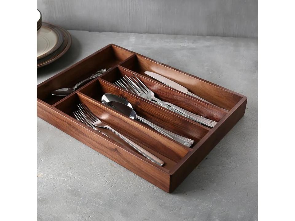 Wooden cutlery organizer tray sitting on a grey countertop with silverware inside.