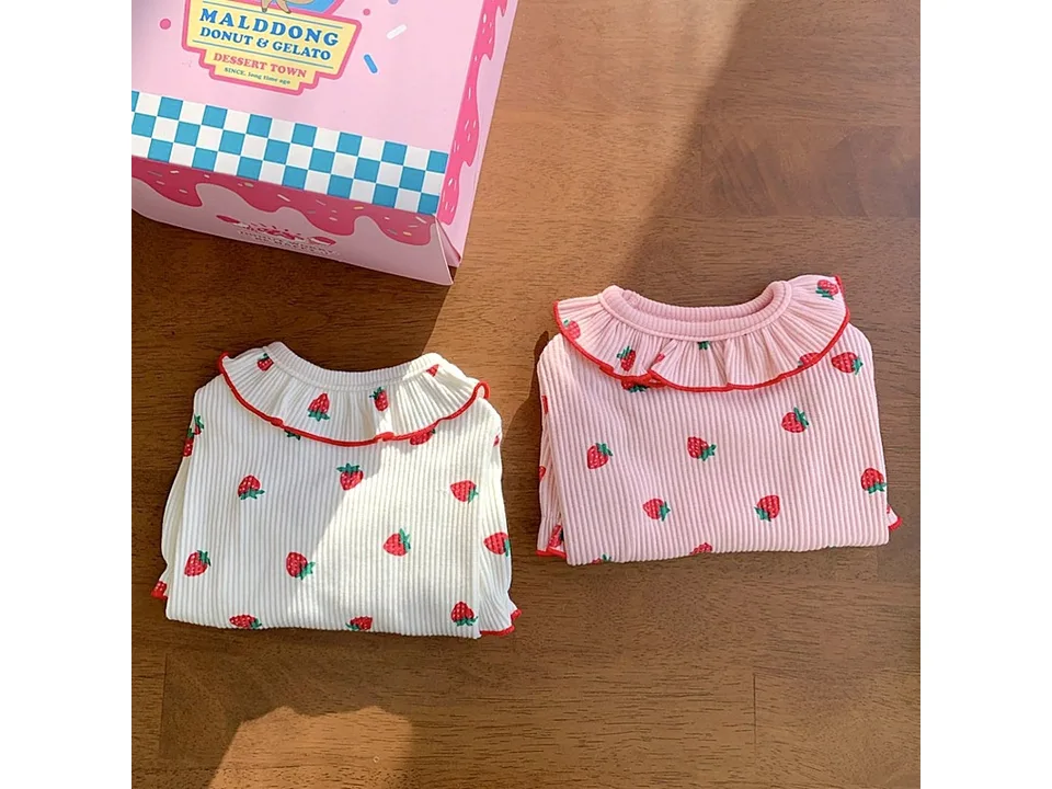 Two strawberry print pet shirts, one white and one pink, laid flat on a wooden surface.
