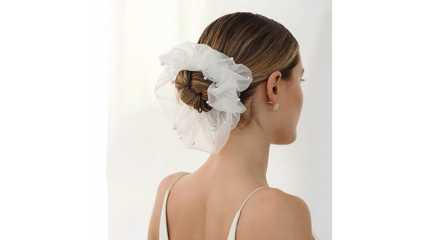 A woman wearing a white mesh hair scrunchie with pearls and a small veil in a bun.