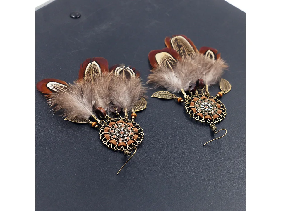 Two bohemian feather dreamcatcher earrings laid out on a dark surface.