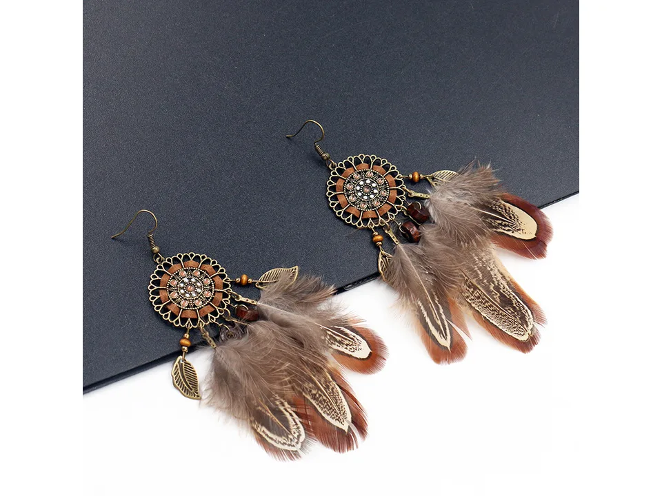 Two bohemian feather dreamcatcher earrings laid out on a dark surface.