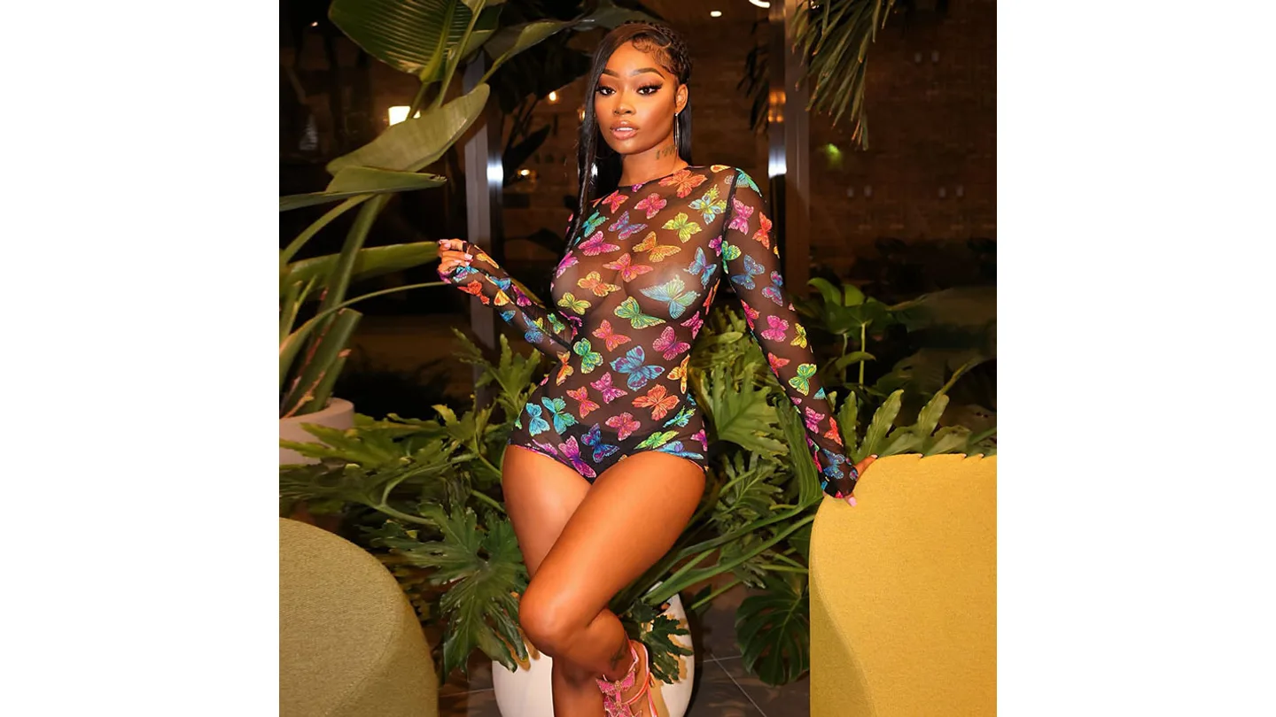 A woman wearing a long-sleeve butterfly print mesh jumpsuit with shorts.