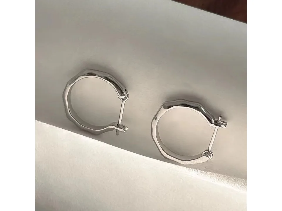 Pair of silver irregular geometric hoop earrings on a white surface.