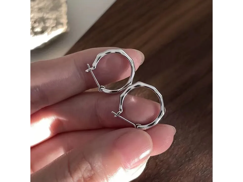 Close-up of silver irregular geometric hoop earrings held between fingers.