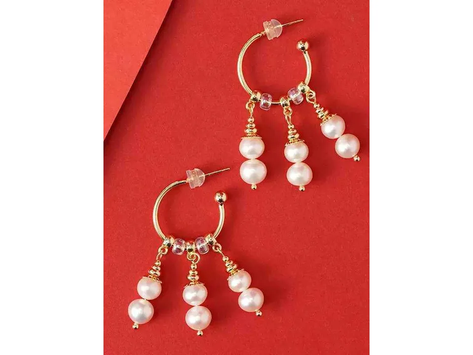 The full pair of gold hoop earrings with pearl dangles laid out on a red surface.