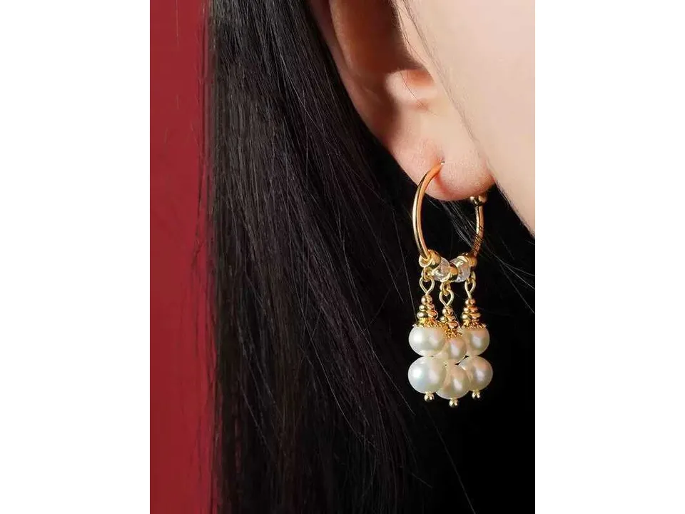A person wearing the gold and pearl dangle hoop earrings.