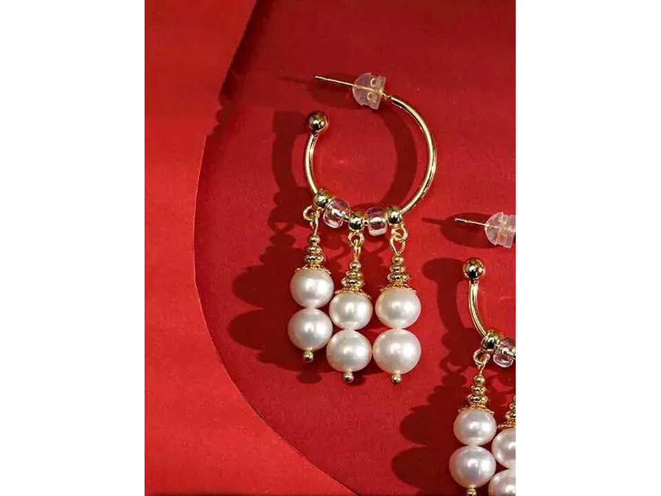 Close-up of gold hoop earrings with dangling pearl charms on a red background.