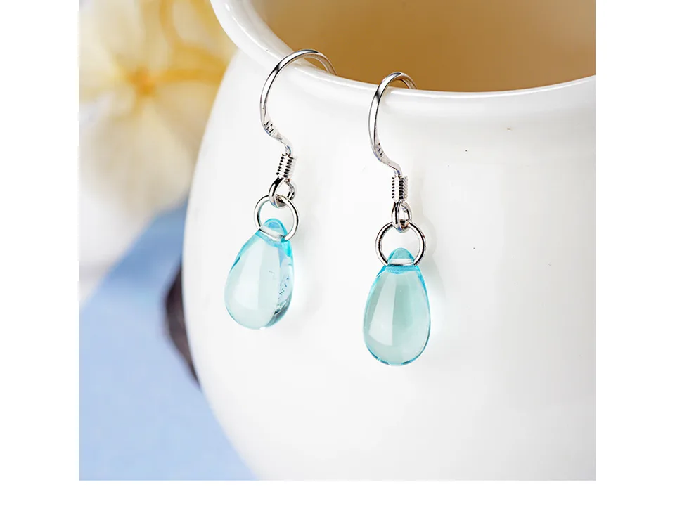 Blue crystal drop earrings hanging on the edge of a white ceramic cup.