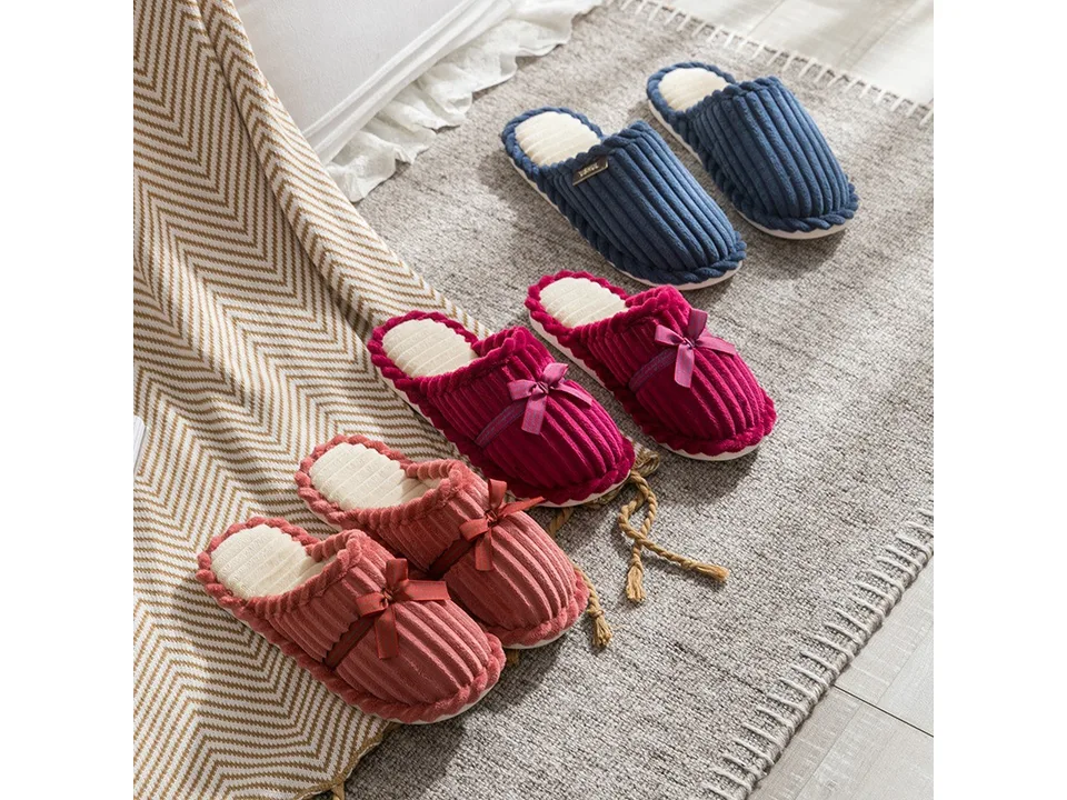 Three pairs of corduroy slippers in blue, magenta, and pink arranged on a rug.