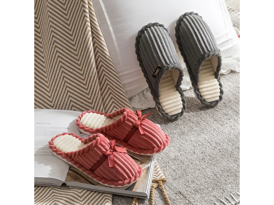 A pair of pink slippers with bows and a pair of grey slippers on a rug.