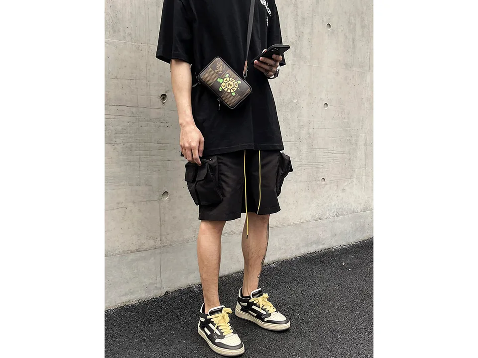 Man wearing black cargo shorts with large side pockets and yellow drawstring.