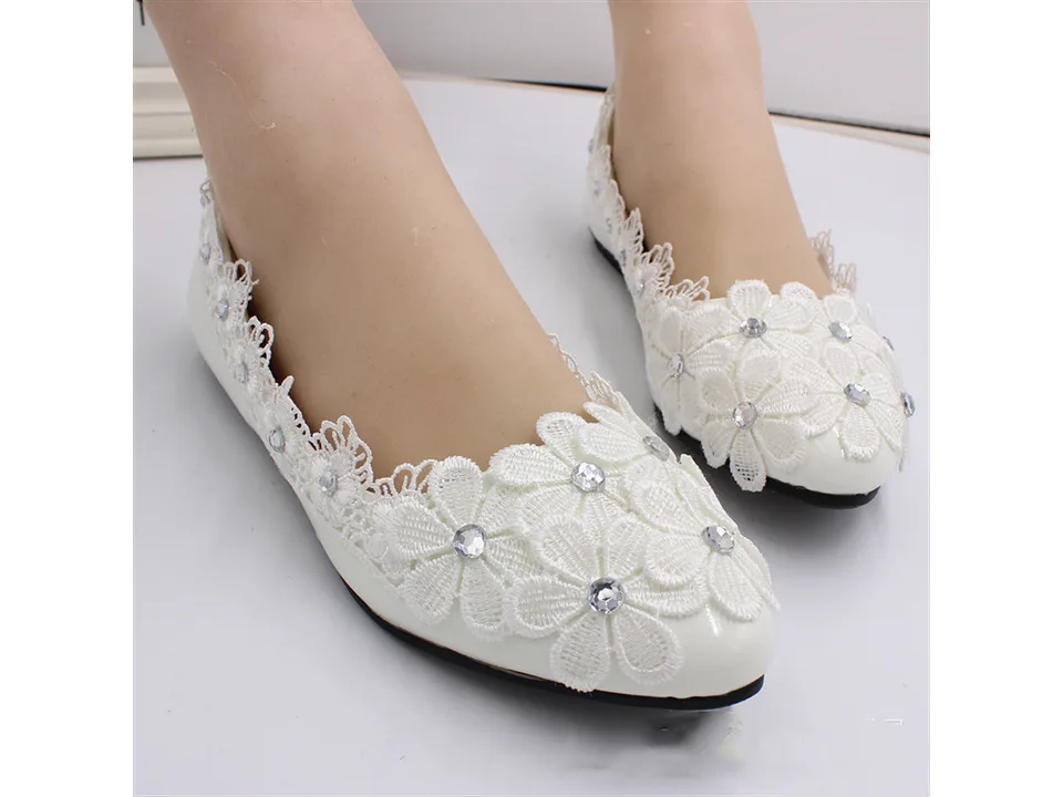 A pair of white lace flat shoes with rhinestone floral embellishments worn on feet.