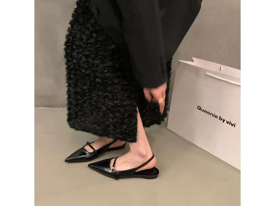 A person wearing black pointed toe slingback sandals with a buckle strap.