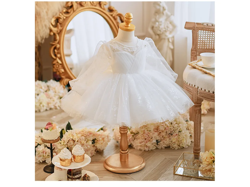 A white long-sleeve princess dress on a mannequin, displayed in a decorated room.